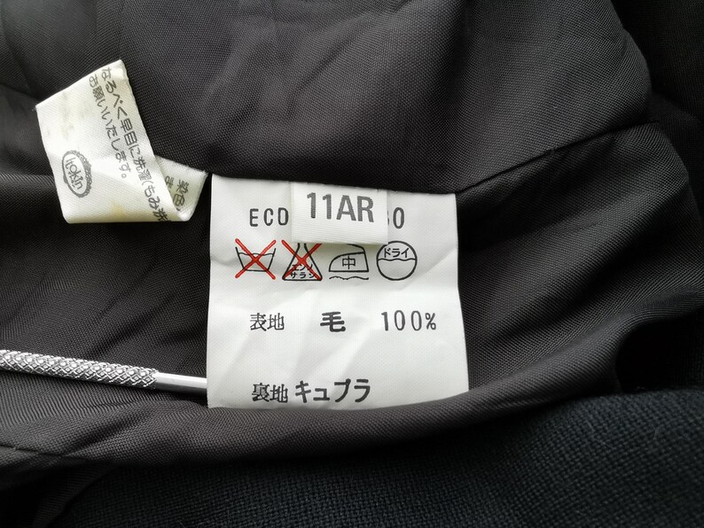 May include: Close-up of a garment's interior, showcasing care instructions and fabric composition. The label reads "ECO 11AR 0" with symbols indicating washing and drying guidelines. The fabric is 100% wool.