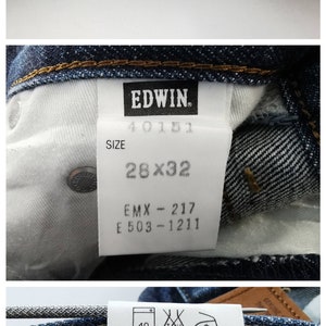 May include: Close-up of blue denim jeans with yellow stitching. The jeans have a label that reads "EDWIN" and size 28x32. The label also includes washing instructions and fabric composition.