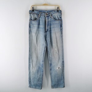 May include: Light blue denim jeans with a faded wash and distressed details, including rips and wear marks. The jeans are hanging on a wooden hanger against a white background. Classic five-pocket design.