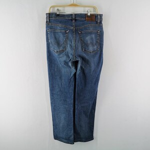 May include: Blue denim jeans hanging on a wooden hanger. The jeans have a classic five-pocket design, a straight leg, and a brown leather patch on the back. The jeans are a medium wash and appear to be unworn.