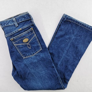 May include: Blue denim jeans with a classic five-pocket design. The jeans feature a straight leg cut, a button and zipper closure, and a small decorative patch on the back pocket. The jeans are made of a durable denim fabric.