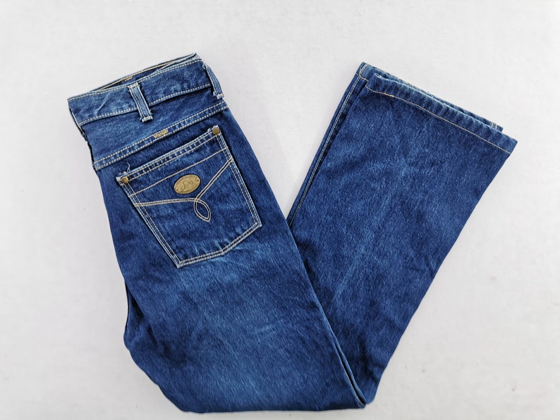 May include: Blue denim jeans with a classic five-pocket design. The jeans feature a straight leg cut, a button and zipper closure, and a small decorative patch on the back pocket. The jeans are made of a durable denim fabric.