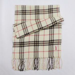 May include: Cream-colored scarf with a plaid pattern in black and red. The scarf has a fringed edge and a small pink logo near the bottom. A portion of the scarf is folded over.