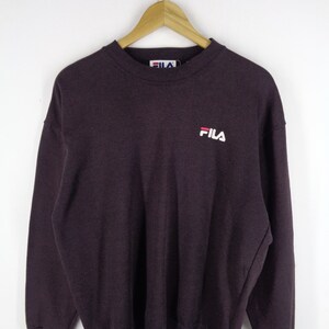Pu&ograve; includere: Una felpa a maniche lunghe con girocollo di colore viola scuro, caratterizzata da colletto, polsini e orlo a coste. Il logo del marchio FILA &egrave; ricamato in bianco e rosso sul petto a sinistra. Un'etichetta bianca con il logo FILA &egrave; visibile sul collo.