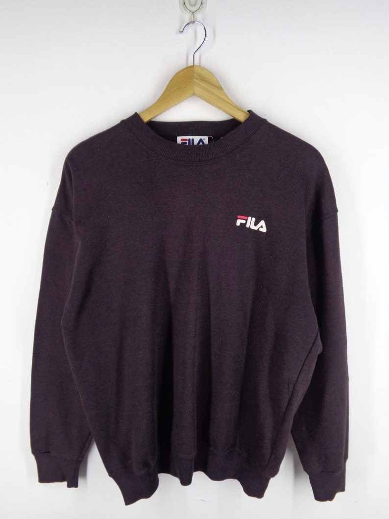 Pu&ograve; includere: Una felpa a maniche lunghe con girocollo di colore viola scuro, caratterizzata da colletto, polsini e orlo a coste. Il logo del marchio FILA &egrave; ricamato in bianco e rosso sul petto a sinistra. Un'etichetta bianca con il logo FILA &egrave; visibile sul collo.