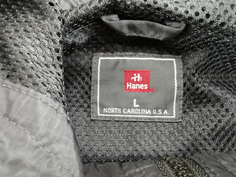 May include: Close-up of a black jacket's interior, featuring a mesh lining and a label. The label, with the Hanes logo in red, indicates size L and states "NORTH CAROLINA U.S.A."