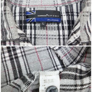 May include: Close-up of a gray, black, and white plaid pajama shirt. The shirt has a collar and a button closure. The label reads "KANGOL SPORT PYJAMAS" and "L". The shirt is made of a soft, comfortable material.