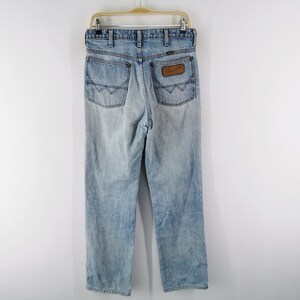 May include: Light blue denim jeans with a faded wash, hanging on a hanger. The jeans feature classic five-pocket styling, a brown leather patch with the brand name, and a straight leg fit. The back pockets have a distinctive design.
