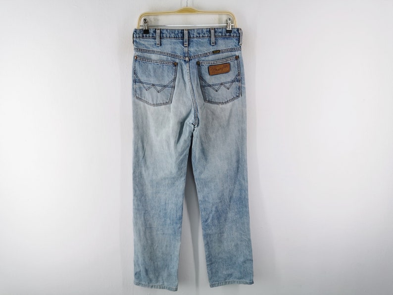 May include: Light blue denim jeans with a faded wash, hanging on a hanger. The jeans feature classic five-pocket styling, a brown leather patch with the brand name, and a straight leg fit. The back pockets have a distinctive design.