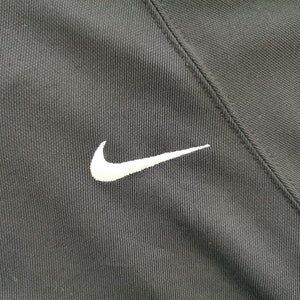 Pu&ograve; includere: Primo piano di tessuto atletico nero con un logo Nike bianco ricamato sul lato sinistro. Il tessuto ha un aspetto strutturato e una cucitura diagonale.