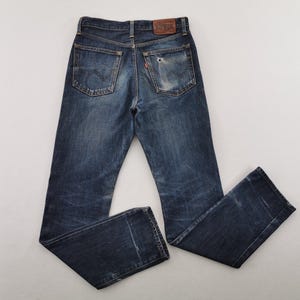 K&ouml;nnte beinhalten: Verblasste blaue Jeans mit einem Used-Look. Die Jeans haben ein klassisches F&uuml;nf-Taschen-Design, einen Lederaufn&auml;her und ein kleines rotes Etikett. Die Jeans liegen flach, wodurch die Ges&auml;&szlig;taschen und die allgemeine Abnutzung zur Geltung kommen.