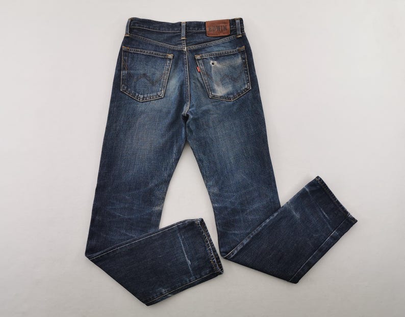 K&ouml;nnte beinhalten: Verblasste blaue Jeans mit einem Used-Look. Die Jeans haben ein klassisches F&uuml;nf-Taschen-Design, einen Lederaufn&auml;her und ein kleines rotes Etikett. Die Jeans liegen flach, wodurch die Ges&auml;&szlig;taschen und die allgemeine Abnutzung zur Geltung kommen.
