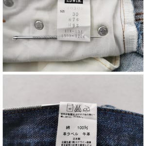 K&ouml;nnte beinhalten: Nahaufnahme der Innenseite einer blauen Jeans. Ein wei&szlig;es Etikett zeigt die Marke "EDWIN" und Gr&ouml;&szlig;enangaben: 30, W76, H93. Die Jeans hat Metallnieten und eine Metallnadel.