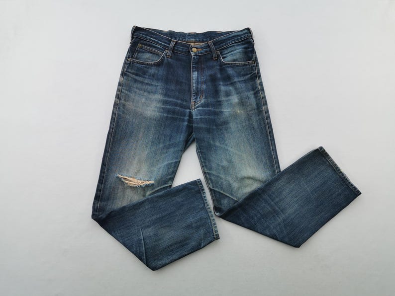 K&ouml;nnte beinhalten: Blaue Jeans aus Denim mit einem Used-Look, mit einem zerrissenen Knie. Die Jeans haben ein klassisches F&uuml;nf-Taschen-Design und einen Knopf- und Rei&szlig;verschluss. Der Denim hat verblasste Bereiche.