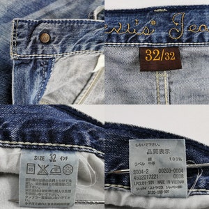 K&ouml;nnte beinhalten: Nahaufnahme einer blauen Jeans mit dem Markennamen "Levi's Jeans" in Goldfaden gestickt. Die Jeans hat ein Gr&ouml;&szlig;enetikett mit der Aufschrift "32/32" und ein Gr&ouml;&szlig;enetikett mit der Aufschrift "SIZE 32 Zoll".