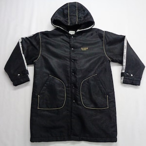 Puede incluir: Chaqueta negra con capucha, costuras doradas y detalles de rayas blancas en las mangas. La chaqueta tiene cierre de botones, dos bolsillos delanteros y la palabra "BASE" en letras doradas.