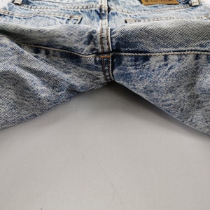 K&ouml;nnte beinhalten: Nahaufnahme einer Jeans aus Acid-Wash-Denim. Die Jeans hat ein hellblaues und wei&szlig;es Marmormuster. Die Ges&auml;&szlig;taschen und der Bund sind sichtbar. Die N&auml;hte sind in einer kontrastierenden orangefarbenen Farbe gehalten.