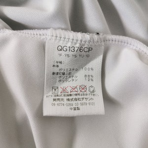 May include: Close-up of a white garment tag with black text. The tag includes the product code "QG1376CP" and fabric composition details: 100% polyester for the main body, 88% polyester for the upper body, and 12% polyurethane. Washing instructions are also present.