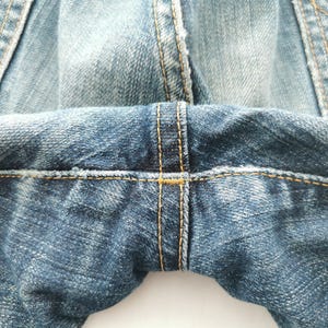 May include: Close-up of blue denim jeans, showcasing the detailed stitching and fabric texture. The image highlights the seams and the overall construction of the garment, emphasizing the quality of the denim.
