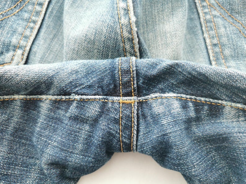 May include: Close-up of blue denim jeans, showcasing the detailed stitching and fabric texture. The image highlights the seams and the overall construction of the garment, emphasizing the quality of the denim.