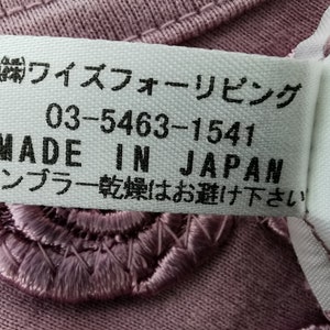 May include: Close-up of a label with Japanese text and the words "MADE IN JAPAN." The label is white with black text and is sewn onto a mauve fabric with embroidered floral details.