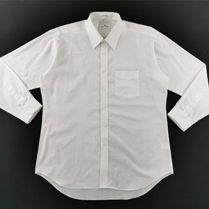 May include: A crisp, white long-sleeve dress shirt with a classic collar and a single chest pocket. The shirt is buttoned up and has buttoned cuffs. The fabric appears to be a smooth, woven material.