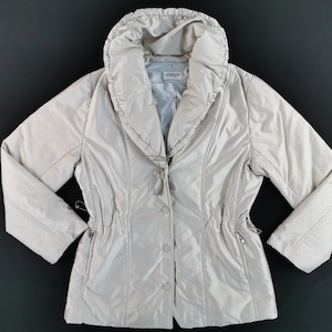 May include: A light beige puffer jacket with a large, rounded collar. The jacket has a drawstring waist, button closure, and zippered pockets. The brand name "LANVIN" is visible on the inner label. The jacket is made of a smooth, shiny material.