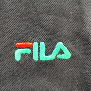 May include: Close-up of a black polo shirt with the embroidered FILA logo. The logo features the word "FILA" in a vibrant green, with the "F" and "A" in a bright green color and the "I" and the horizontal line of the "L" in red and orange.