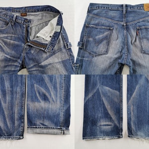 K&ouml;nnte beinhalten: Blaue Jeans aus Denim mit verwaschener Optik und Used-Details. Die Jeans haben einen Knopf- und Rei&szlig;verschluss, mehrere Taschen und einen Lederaufn&auml;her auf der R&uuml;ckseite. Die Jeans werden aus verschiedenen Blickwinkeln gezeigt.