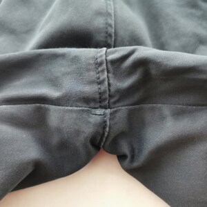 May include: Close-up of the crotch area of dark gray pants. The fabric is a solid color with visible stitching along the seams. The pants appear to be made of a durable material, suitable for everyday wear.