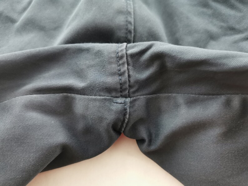 May include: Close-up of the crotch area of dark gray pants. The fabric is a solid color with visible stitching along the seams. The pants appear to be made of a durable material, suitable for everyday wear.