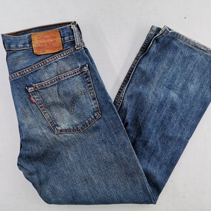 May include: Blue denim jeans with a classic five-pocket design. The jeans feature a faded wash and a red Levi's tag on the back pocket. The jeans are folded and laid flat.