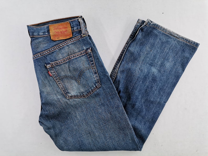 May include: Blue denim jeans with a classic five-pocket design. The jeans feature a faded wash and a red Levi's tag on the back pocket. The jeans are folded and laid flat.