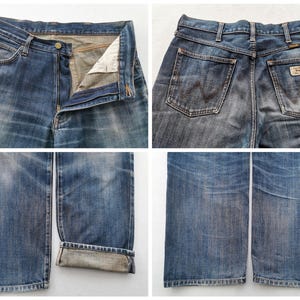 K&ouml;nnte beinhalten: Nahaufnahmen von blauen Jeans. Die Jeans sind verblichen und abgenutzt, mit sichtbaren Details der Taschen, des Knopfverschlusses und des Wrangler-Markenlabels. Der Denim hat einen klassischen, Vintage-Look.