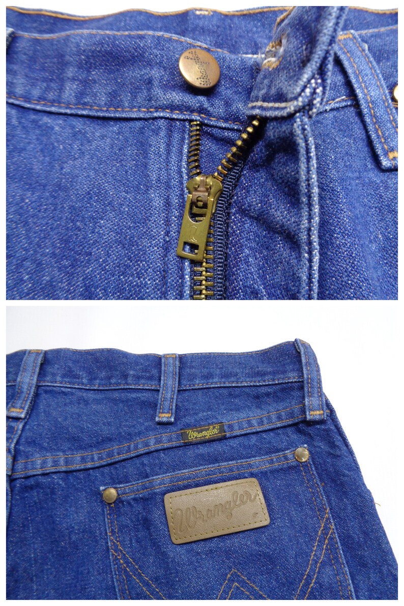 May include: Close-up of blue denim jeans. The jeans feature a brass zipper, a button closure, and the Wrangler logo on a brown leather patch. The stitching is in a contrasting yellow-brown color.