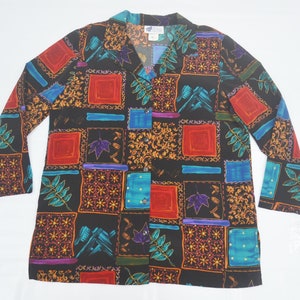 May include: A long-sleeved button-down shirt with a colorful patchwork design. The shirt features a black background with squares of red, blue, teal, and gold patterns. The shirt has a V-neck collar and is made of a lightweight fabric.