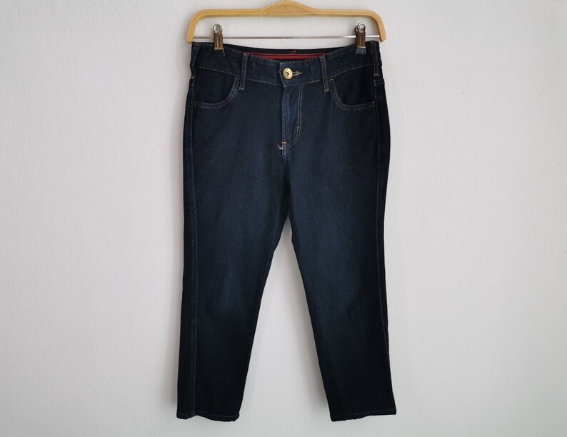 K&ouml;nnte beinhalten: Dunkelblaue Jeans an einem Holzb&uuml;gel. Die Jeans haben ein klassisches F&uuml;nf-Taschen-Design mit Knopf- und Rei&szlig;verschluss. Die Jeans sind im Straight-Leg-Stil gehalten.