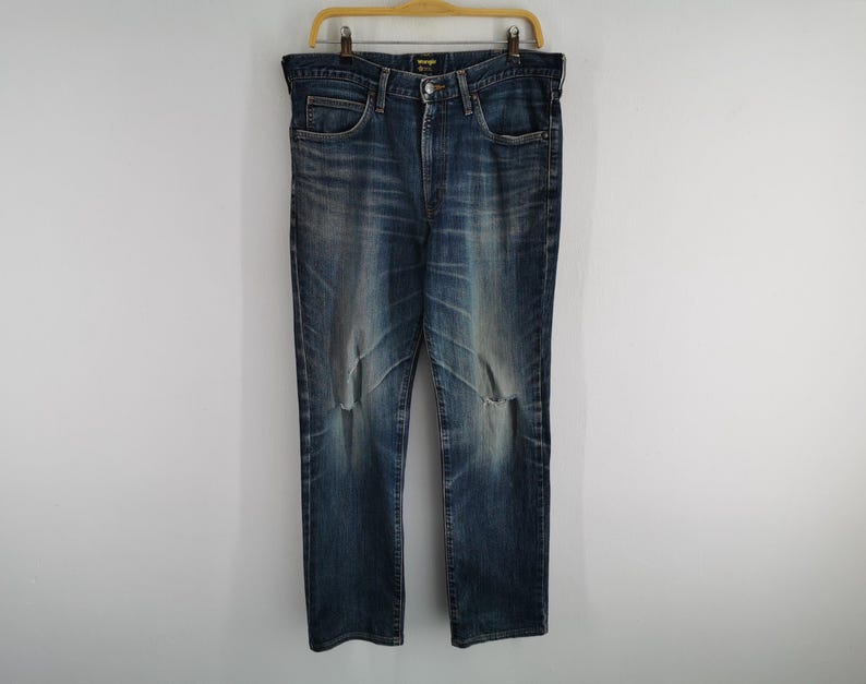 May include: Blue denim jeans with a faded wash and distressed details, hanging on a wooden hanger. The jeans have a classic five-pocket design and a button and zipper closure. The jeans are a size 36.