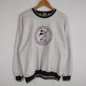 Puede incluir: Sudadera gris claro con ribetes negros y gris oscuro. La parte delantera presenta un gráfico circular con un personaje de dibujos animados y el texto "Osprey Ridge Oak Trail Magnolia Palm Lake Buena Vista Eagle Pines".