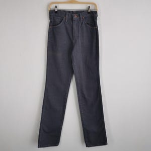 May include: Dark blue denim jeans hanging on a wooden hanger. The jeans have a classic five-pocket design with a button and zipper closure. The pants are straight-legged and appear to be unworn.