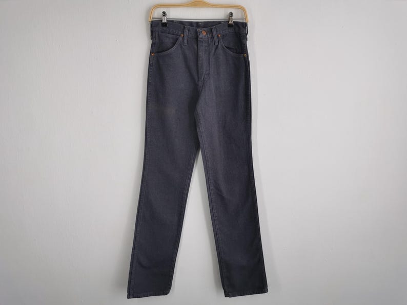 May include: Dark blue denim jeans hanging on a wooden hanger. The jeans have a classic five-pocket design with a button and zipper closure. The pants are straight-legged and appear to be unworn.