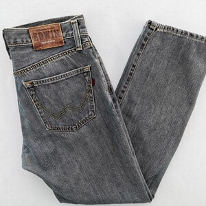 May include: Gray denim jeans with a classic five-pocket design. Features a brown leather patch with the brand name and a red tag on the back pocket. The jeans are made of a durable fabric and have a straight leg cut.