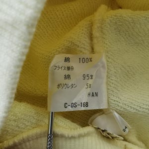 May include: Close-up of a fabric tag with Japanese text indicating the material composition: 100% cotton, 95% cotton, and 5% polyurethane. The tag is attached to a light yellow fabric. The tag also has the text "HAN" and "C-OS-168".