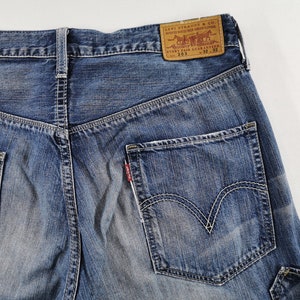 K&ouml;nnte beinhalten: Nahaufnahme der R&uuml;ckseite einer blauen Jeans. Die Jeans hat eine verwaschene Optik, wei&szlig;e N&auml;hte und ein klassisches F&uuml;nf-Taschen-Design. Ein braunes Lederpatch mit dem Levi Strauss & Co. Logo ist sichtbar, zusammen mit der Gr&ouml;&szlig;e 32x32.
