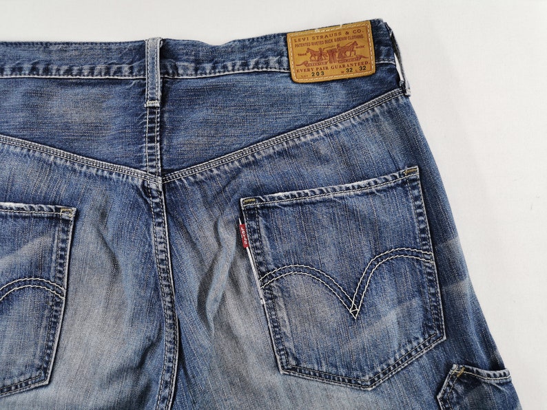 K&ouml;nnte beinhalten: Nahaufnahme der R&uuml;ckseite einer blauen Jeans. Die Jeans hat eine verwaschene Optik, wei&szlig;e N&auml;hte und ein klassisches F&uuml;nf-Taschen-Design. Ein braunes Lederpatch mit dem Levi Strauss & Co. Logo ist sichtbar, zusammen mit der Gr&ouml;&szlig;e 32x32.