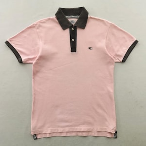 May include: A short-sleeved polo shirt in light pink with a dark brown collar and sleeve cuffs. The shirt features a dark brown button placket with two light-colored buttons and a small embroidered logo on the left chest. The hem is straight.
