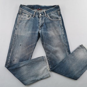 May include: Faded blue denim jeans with a classic five-pocket design. The jeans have a button and zip closure, with a distressed look and slight paint marks. The leg openings are frayed. A casual, everyday wear item.