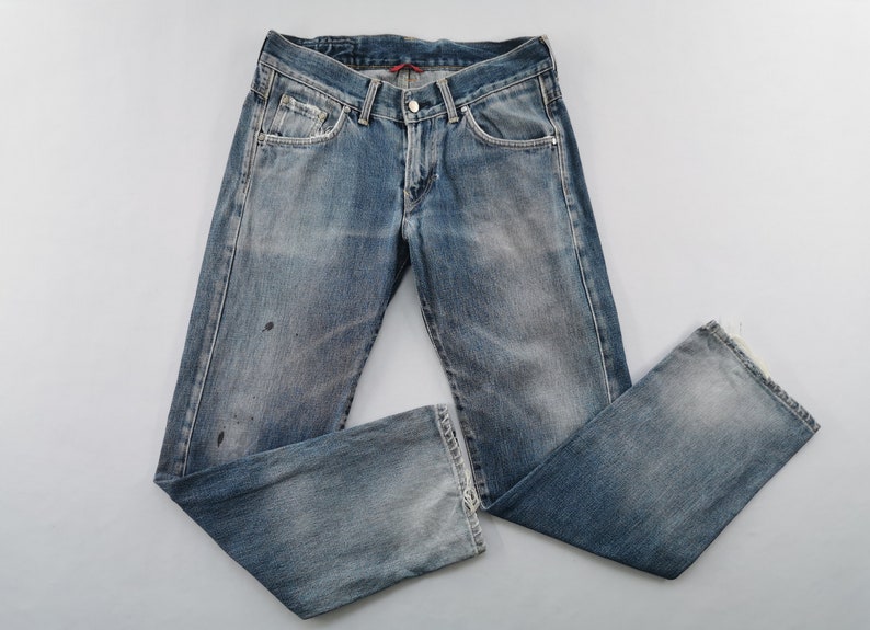 May include: Faded blue denim jeans with a classic five-pocket design. The jeans have a button and zip closure, with a distressed look and slight paint marks. The leg openings are frayed. A casual, everyday wear item.