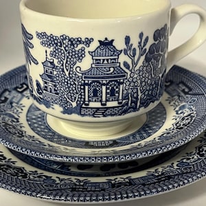 May include: A blue and white porcelain teacup and saucer set with a willow pattern design. The set features a traditional Chinese landscape with a pagoda, trees, and a river.