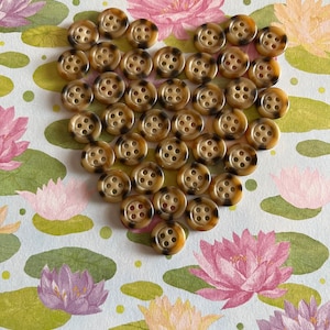 May include: A heart shape made of 30 brown and black patterned buttons. The buttons are arranged in a heart shape on a white background with a floral pattern.